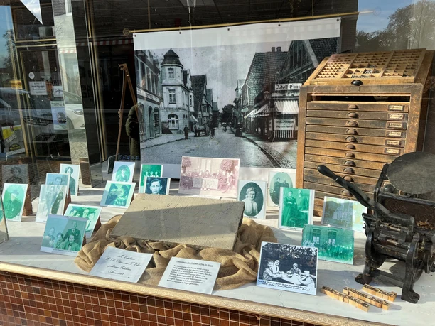 Eine Schaufensterpräsentation zeigt historische Fotografien und Druckwerkzeuge, die an eine Druckerei erinnern.