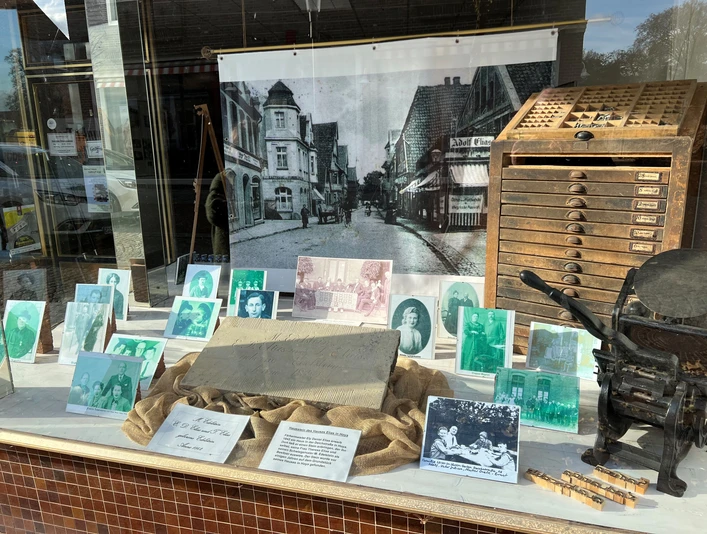 Eine Schaufensterpräsentation zeigt historische Fotografien und Druckwerkzeuge, die an eine Druckerei erinnern.