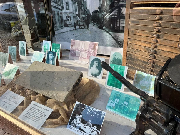 IG Synagoge Fotografien vor einem antiken Schubladenschrank in einem Schaufenster, darunter ein gravierter Stein.