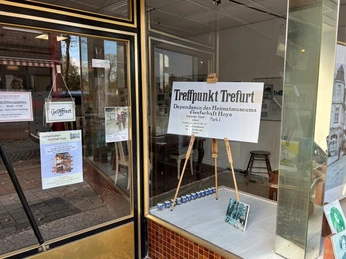 IG Synagoge Ein Fenster eines Museums zeigt Info-Plakate und Modelle. Drinnen befinden sich Stühle und Ausstellungsstücke.