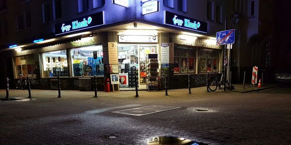 Jazz Kiosk Der Jazz-Kiosk bei Nacht zeigt ein beleuchtetes Geschäft in urbaner Umgebung mit reflektierendem Schaufenster und Regenpfütze.The jazz kiosk at night shows an illuminated store in an urban environment with a reflective shop window and a puddle of rain.