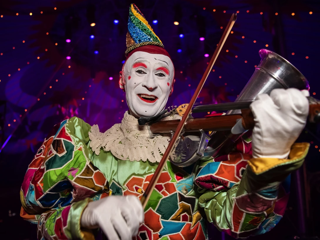 roncalli_gensi_-_circus-theater_roncalli_2022.jpg Clown spielt ausgelassen Violine unter buntem Zeltlicht, strahlt Freude und Magie der Zirkuswelt aus.Clown plays the violin under colorful tent lights, radiating the joy and magic of the circus world.Klovnen spiller violin under farverige teltlamper og udstråler cirkusverdenens glæde og magi.Clown speelt viool onder kleurrijke tentverlichting, die de vreugde en magie van de circuswereld uitstraalt.