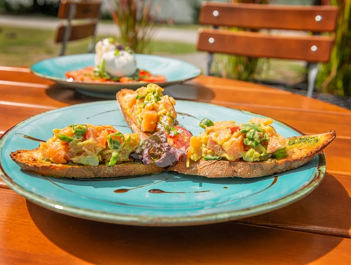 Außenterrasse des Café-Restaurant am Rubbenbruchsee Ein Teller mit belegten Brotscheiben, üppig garniert mit frischen Tomaten, Paprika und Kräutern.A plate with slices of bread, lavishly garnished with fresh tomatoes, peppers and herbs.En tallerken med brødskiver, overdådigt pyntet med friske tomater, peberfrugter og krydderurter.Een bord met sneetjes brood, rijkelijk gegarneerd met verse tomaten, paprika en kruiden.