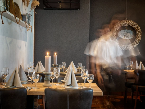 Innenraum Café-Restaurant am Rubbenbruchsee Elegantes Café-Restaurant mit gedeckten Tischen, Kerzenlicht und verschwommenen Silhouetten von Gästen.