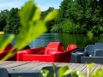 Bootverleih am Rubbenbruchsee Tretboote in kräftigem Rot und Schwarz liegen an einem Steg am Ufer eines von Bäumen umgebenen Sees.Pedal boats in bright red and black are moored on a jetty on the shore of a lake surrounded by trees.Pedalbåde i knaldrødt og sort ligger fortøjet på en anløbsbro ved bredden af en sø omgivet af træer.Waterfietsen in felrood en zwart liggen aangemeerd aan een steiger aan de oever van een meer omringd door bomen.