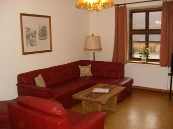 Burg Borgholz - Wohnbereich Roter Ledersessel und -sofa gruppiert um einen Holztisch, neben Fenster mit Vorhängen und Lampe.