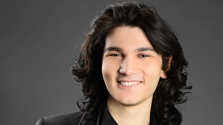 Weltklassik: Kaan Baysal Lächelndes Porträt des Pianisten Kaan Baysal mit dunklem Haar vor grauem Hintergrund.