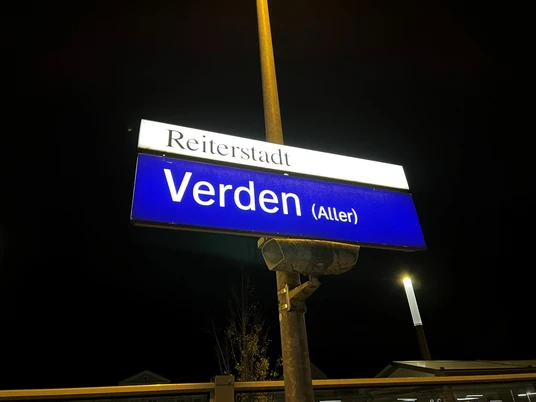Ein nachts beleuchtetes Bahnhofsschild mit der Aufschrift "Reiterstadt Verden (Aller)".