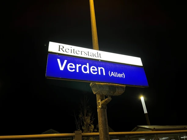 Ein nachts beleuchtetes Bahnhofsschild mit der Aufschrift "Reiterstadt Verden (Aller)".