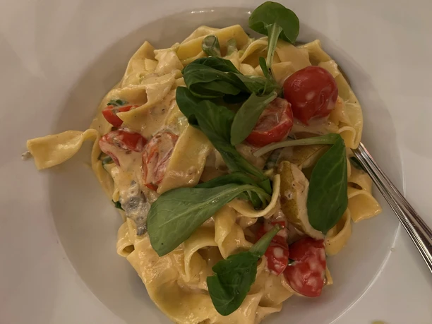 A plate of tagliatelle garnished with fresh rocket and cherry tomatoes in a creamy sauce.