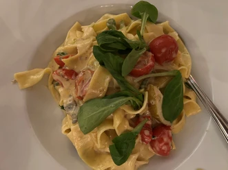 Nudelgericht Ein Teller mit Bandnudeln, garniert mit frischem Rucola und Kirschtomaten in einer cremigen Sauce.