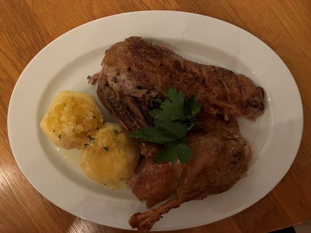 Fleischgericht Geröstete Gänsekeule mit zwei Kartoffelknödeln, serviert auf einem weißen ovalen Teller.