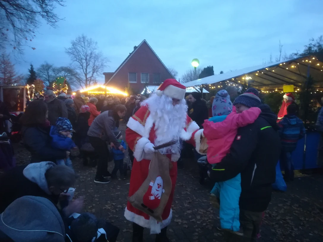 Weihnachtsmarkt in Apen.jpg Weihnachtsmann verteilt Geschenke an Kinder auf belebtem Markt mit Lichtern und Buden in Apen.Santa hands out presents to children at a lively market with lights and stalls in Apen.Julemanden deler gaver ud til børn på et livligt marked med lys og boder i Apen.De kerstman deelt cadeautjes uit aan kinderen op een levendige markt met lichtjes en kraampjes in Apen.