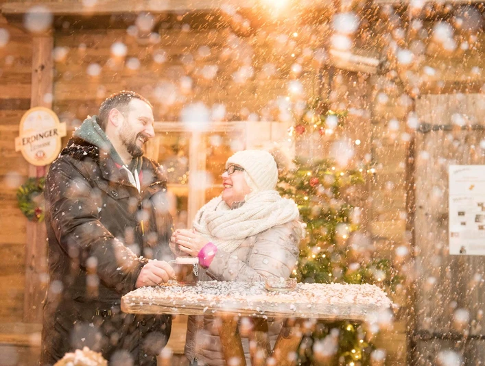 markt-im-advent-schneehuette.jpg Eine Frau und ein Mann lachen an einem Holztisch im Schnee, umgeben von warmem Licht und Winterdekorationen.A woman and a man laugh at a wooden table in the snow, surrounded by warm light and winter decorations.En kvinde og en mand griner ved et træbord i sneen, omgivet af varmt lys og vinterdekorationer.Een vrouw en een man lachen aan een houten tafel in de sneeuw, omringd door warm licht en winterse decoraties.