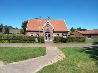IMG20220811124054.jpg Das Bild zeigt ein charmantes Backsteinhaus mit rotem Ziegeldach inmitten einer grünen Wiese unter einem strahlend blauen Himmel. Vor dem Haus sind gepflegte Büsche und ein gepflasterter Weg sichtbar, der zur Eingangstür führt.