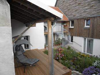 Garten und Terrasse Geräumige Terrasse mit Liegestühlen, umgeben von einem bunten Blumengarten und rustikaler Architektur.