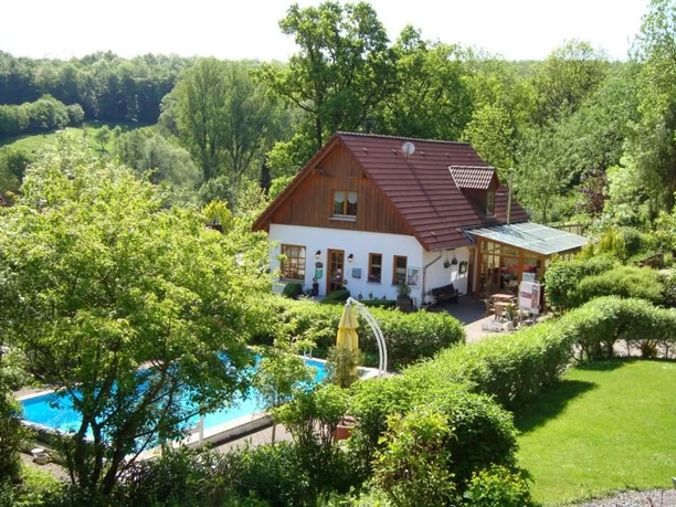Poolansicht Ein Haus im Grünen mit Pool und Terrasse, umgeben von Bäumen und einem gepflegten Garten.