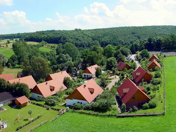 Luftansicht Feriendorf Luftaufnahme eines Feriendorfes mit traditionellen Holzdächern, umgeben von Wäldern und Wiesen.