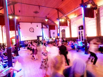 lindy-hop-2.jpg Tanzpaar in einem historischen Saal mit Holzboden; verschwommen in schwungvollem Lindy-Hop-Tanz.