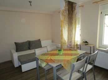 Ferienwohnung Abenteuerland - Essecke Essecke mit Holztisch, vier Stühlen und Sofa vor heller Wand; Fenster mit Sonnenlicht.