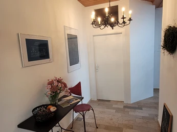 HofHausNr3 - Foyer Ein einladendes Foyer mit einem Tisch, darauf Blumenarrangement, Zeitschriften und Obstkorb.