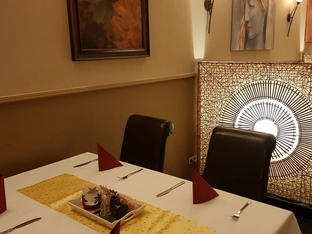 20221121_183951.jpg Ein elegant gedeckter Tisch mit einer weißen Tischdecke, vier Rote servierten, Gabel und Messer und einer gelben länglichen Tischdecke darauf steht ein Gesteck. In einem warm beleuchtetem Ambiente, verziert mit Kunstwerken an den Wänden.