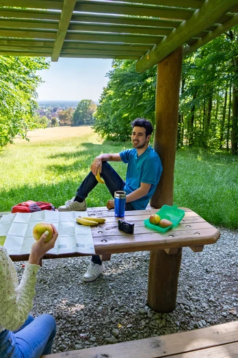 Halle-Hörstation-Teutoburger-Wald-Tourismus-Patrick-Gawandtka-090_lowres.jpg Zwei Personen sitzen an einem Holztisch unter einem hölzernen Pavillon im sommerlichen Wald.