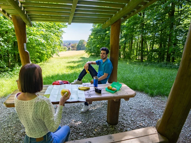 Halle-Hörstation-Teutoburger-Wald-Tourismus-Patrick-Gawandtka-090_lowres.jpg Zwei Personen sitzen an einem Holztisch unter einem hölzernen Pavillon im sommerlichen Wald.