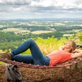 Werther-Hermannshöhen-Teutoburger-Wald-Tourismus-D-Ketz-087.jpg Frau liegt entspannt in der Hängematte mit Blick auf die hügelige Landschaft des Teutoburger Waldes.