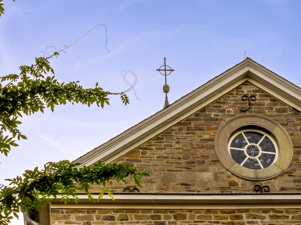 Kirche Delling Steinwand-Fassade eines Gebäudes mit rundem Fenster und Kreuz auf dem Giebel, blauer Himmel.