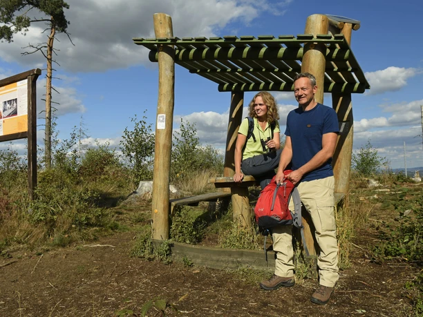 Ein Paar steht mit Wanderausrüstung bei einer hölzernen Raststation im Teutoburger Wald.