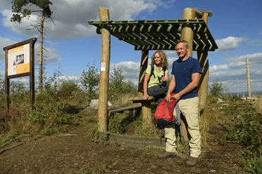 Steinhagen-Hörstation-Teutoburger-Wald-Tourismus-F-Grawe (3)_klein.jpg Ein Paar steht mit Wanderausrüstung bei einer hölzernen Raststation im Teutoburger Wald.
