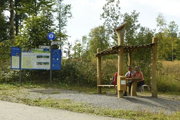 Bad Driburg-Hoerstation-Teutoburger-Wald-Tourismus-F-Grawe (32)_Klein.jpg Zwei Personen sitzen unter einer hölzernen Überdachung neben einer Infotafel im Teutoburger Wald.