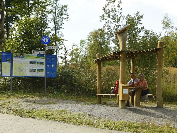 Bad Driburg-Hoerstation-Teutoburger-Wald-Tourismus-F-Grawe (32)_Klein.jpg Zwei Personen sitzen unter einer hölzernen Überdachung neben einer Infotafel im Teutoburger Wald.