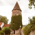 Wehrturm Wehrturm mit runder, begrünten Fassade und spitzem Dach, umgeben von Häusern und Bäumen.