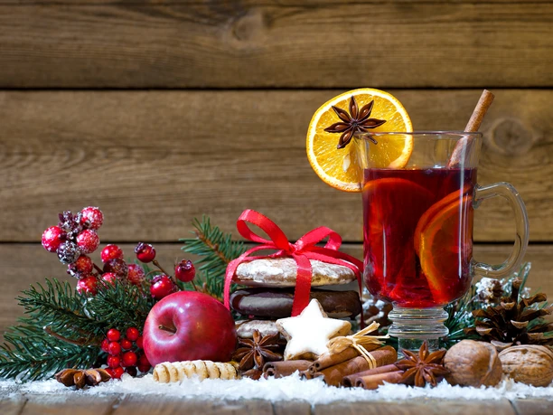 Ein Glas heißer Punsch mit Orangenscheibe, weihnachtlichem Gebäck und Gewürzen auf Holztisch dekoriert.