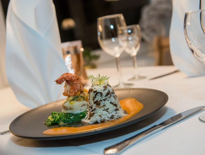 Köstlich angerichtetes Gourmetgericht mit Garnelen, Reis und Sauce auf einem elegant gedeckten Tisch.