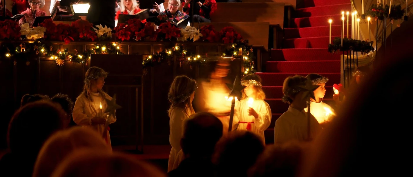Weihnachtskonzert mit Chor auf festlich geschmückter Bühne; Kinder im Engel-Kostüm tragen Kerzen.