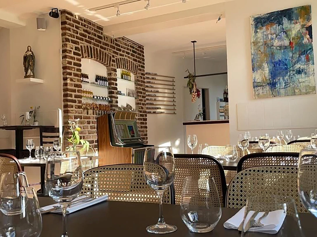 Mit Geschirr, Servietten und Gläsern gedeckte Tische, Stühle, buntes Bild an einer Wand und eine weitere Wand ist eine Steinwand.