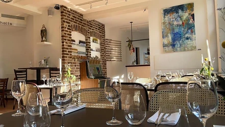 O'FRÀ Pizzabar Mit Geschirr, Servietten und Gläsern gedeckte Tische, Stühle, buntes Bild an einer Wand und eine weitere Wand ist eine Steinwand.