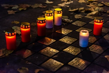 Musterbild Stolpersteine Stolpersteine mit Kerzenlicht umgeben, erinnern im Abendlicht an Holocaust-Opfer, umgeben von Laub.