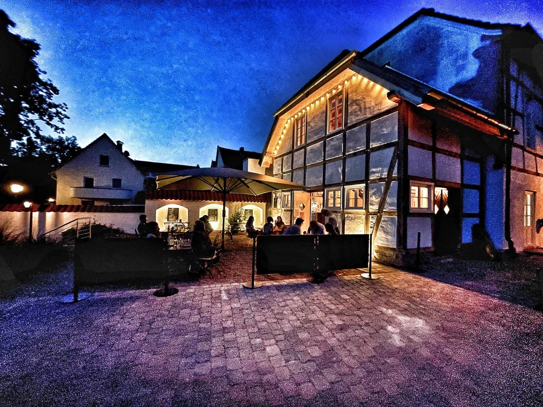 Maedchenschule Ein traditionelles Fachwerkgebäude mit gemütlicher Außenbeleuchtung und Gästen auf der Terrasse bei Dämmerung.