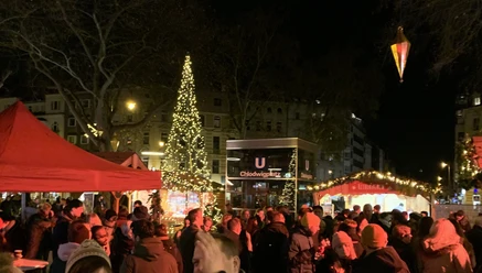 Menschen auf beleuchtetem Weihnachtsmarkt am Chlodwigplatz mit geschmücktem Baum