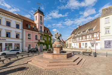 Marktplatz Wurzen Historischer Marktplatz mit Brunnen, umgeben von alten Gebäuden und einer Kirche unter blauem Himmel.