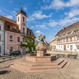 Marktplatz Wurzen Historischer Marktplatz mit Brunnen, umgeben von alten Gebäuden und einer Kirche unter blauem Himmel.