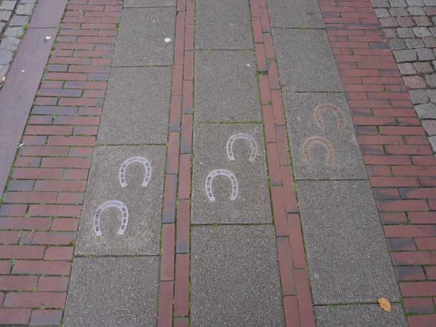 Hufeisenspur Verden Pflasterweg mit eingelegten Hufeisenmustern in Reihen, umgeben von rotbraunen Pflastersteinen.