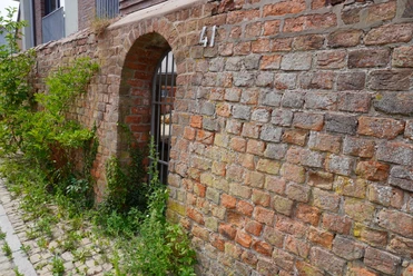 Alte Stadtmauer Verden Alte Backsteinmauer mit Torbogen und Hausnummer 41, überwuchert von Grünpflanzen an einem gepflasterten Weg.
