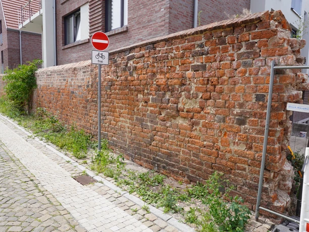 Alte Stadtmauer in Verden mit verwitterten Ziegeln entlang einer gepflasterten Straße.