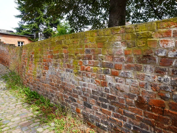 A historic brick wall in Verden, covered with moss and surrounded by cobblestones.