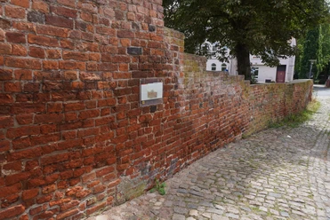 Rote Backsteinmauer aus dem Mittelalter in Verden, durchzogen von einem gepflasterten Weg.